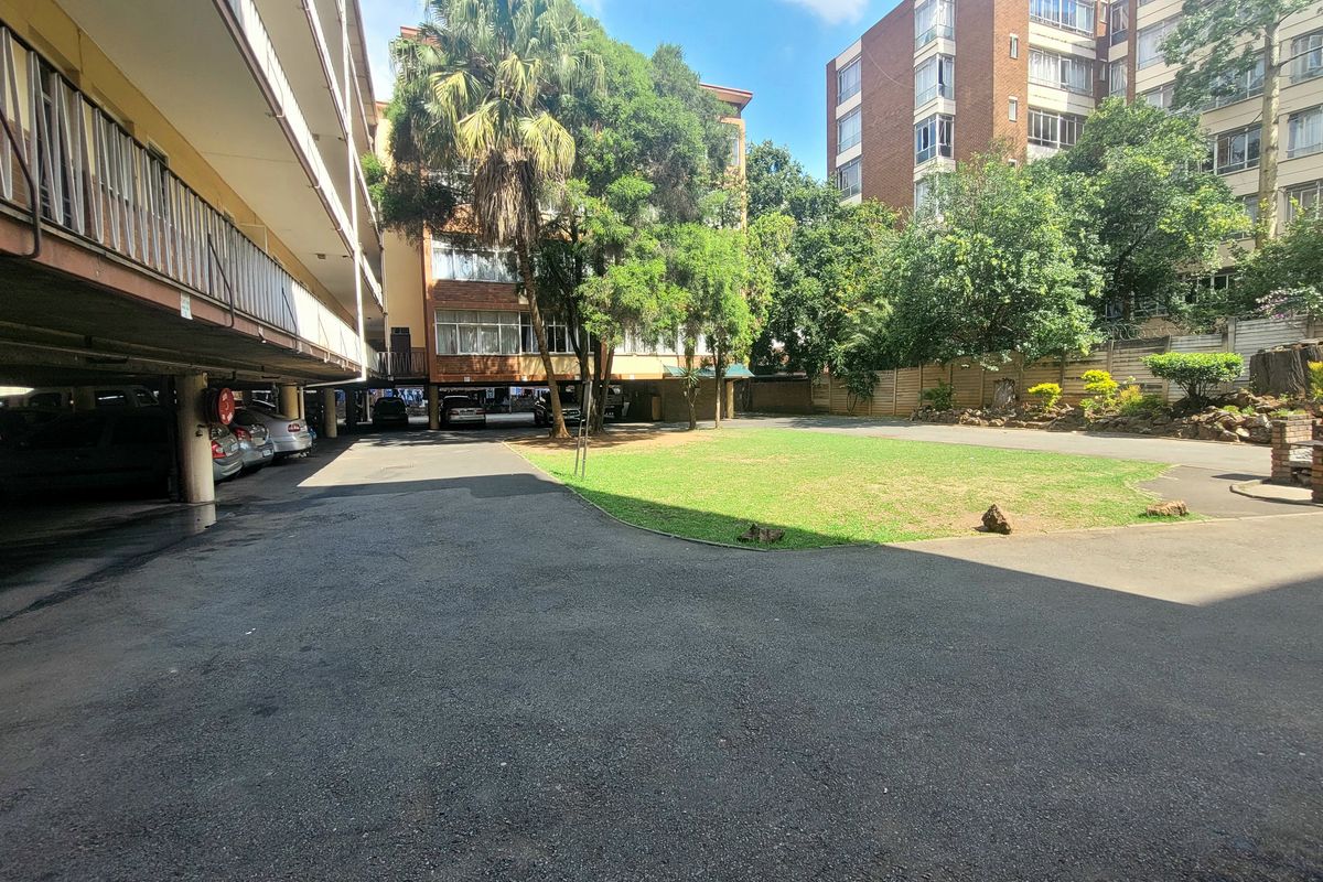 View of the communal rear courtyard featuring an asphalt driveway, covered parking bays, and a landscaped garden area within the apartment complex.