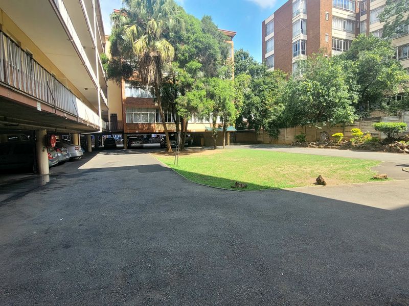 View of the communal rear courtyard featuring an asphalt driveway, covered parking bays, and a landscaped garden area within the apartment complex.