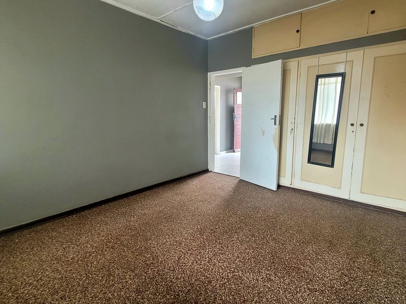 An empty bedroom featuring built-in cupboards with overhead storage, carpeted flooring, and neutral wall tones, offering a blank canvas for renovation.