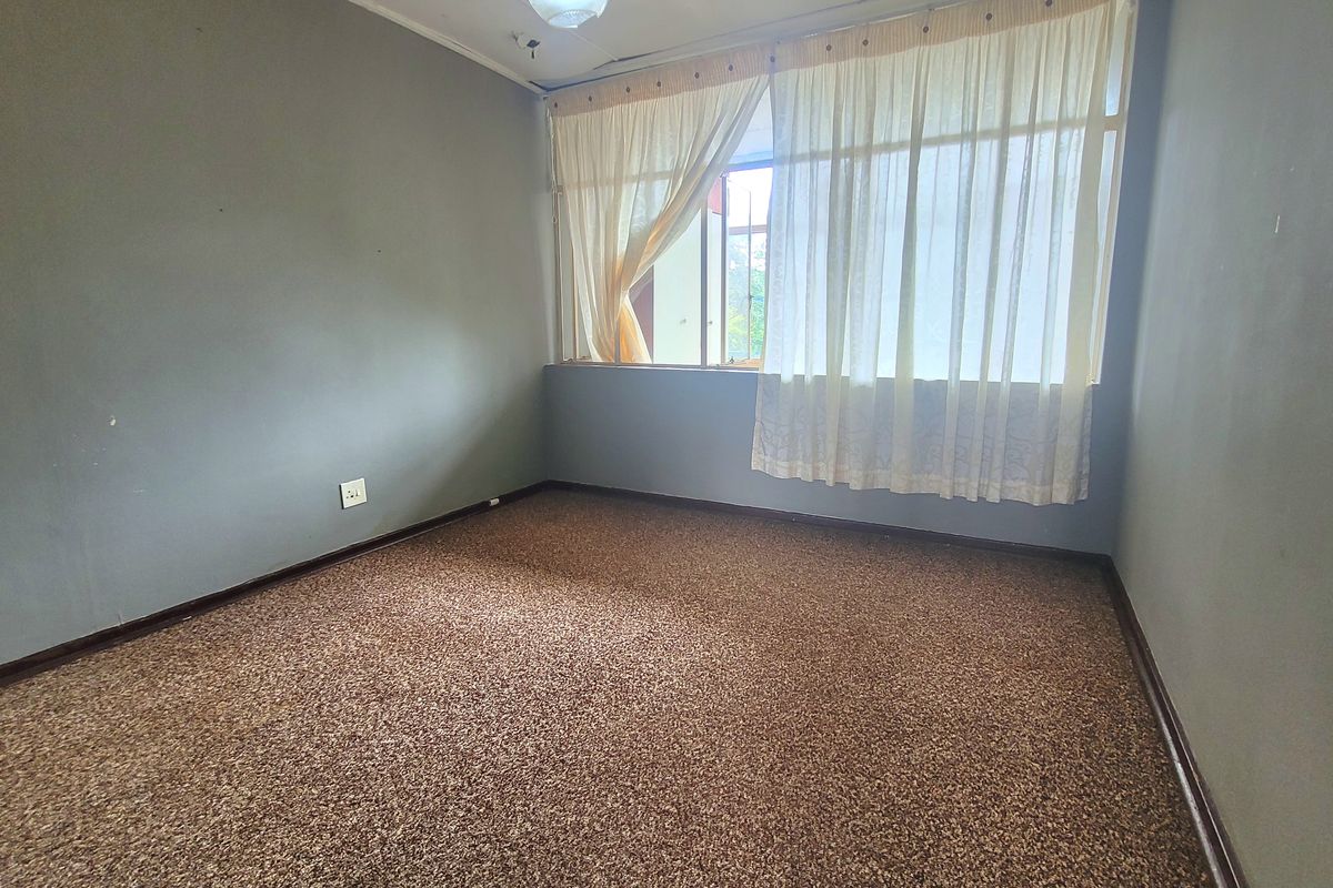 An empty bedroom featuring carpet flooring and a large window, requiring cosmetic updates to the ceiling and flooring.