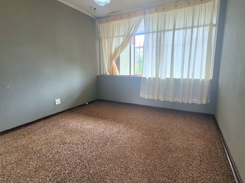 An empty bedroom featuring carpet flooring and a large window, requiring cosmetic updates to the ceiling and flooring.