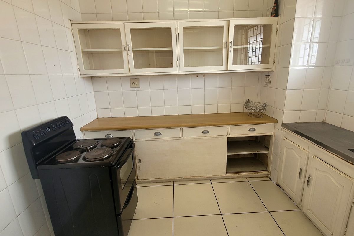 A dated kitchen featuring white cabinetry, tiled walls and flooring, and a functional layout with built-in storage and a sink area.