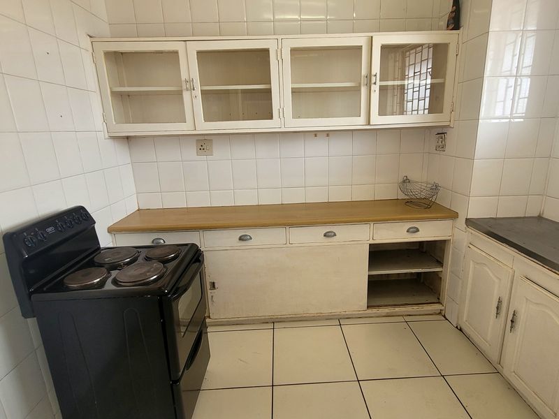 A dated kitchen featuring white cabinetry, tiled walls and flooring, and a functional layout with built-in storage and a sink area.