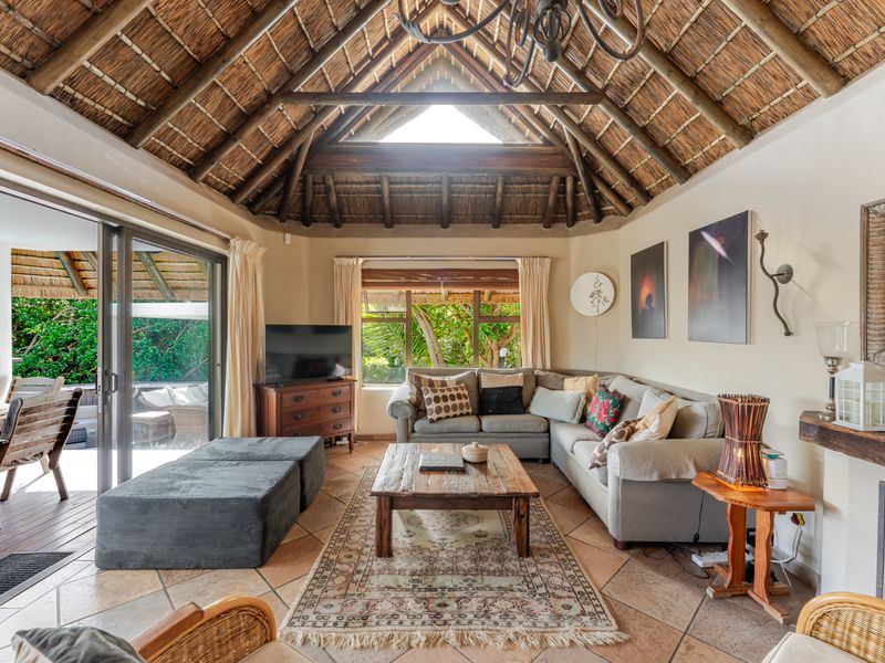 Spacious living room featuring a high vaulted thatched ceiling with exposed timber trusses, tiled floors, and large sliding doors opening to an outdoor patio.