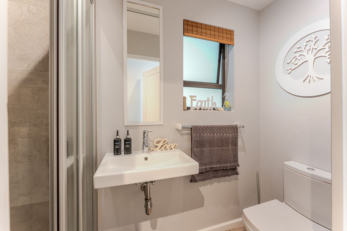 A clean and modern bathroom featuring a wall-mounted basin, a shower enclosure, and a toilet, finished with neutral tones and functional fixtures.