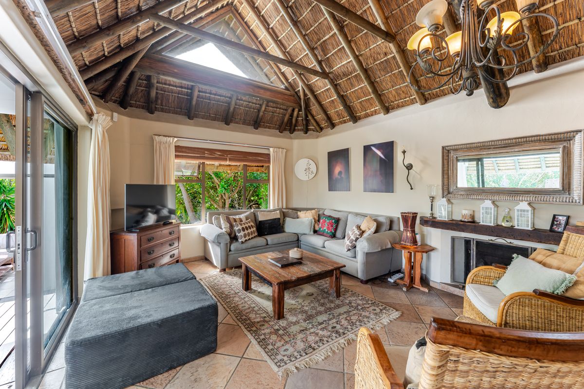 Spacious living room featuring a high vaulted thatched ceiling with exposed timber rafters, a fireplace, and terracotta flooring with access to the patio.