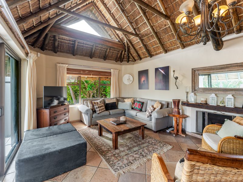 Spacious living room featuring a high vaulted thatched ceiling with exposed timber rafters, a fireplace, and terracotta flooring with access to the patio.