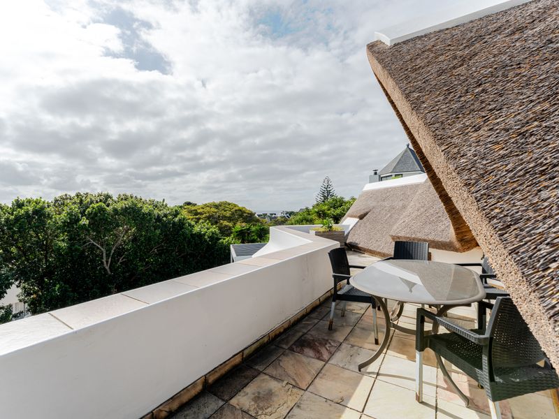 A spacious balcony featuring stone tiling, a protective parapet wall, and a distinctive thatched roof overhang, offering an elevated outdoor living space.