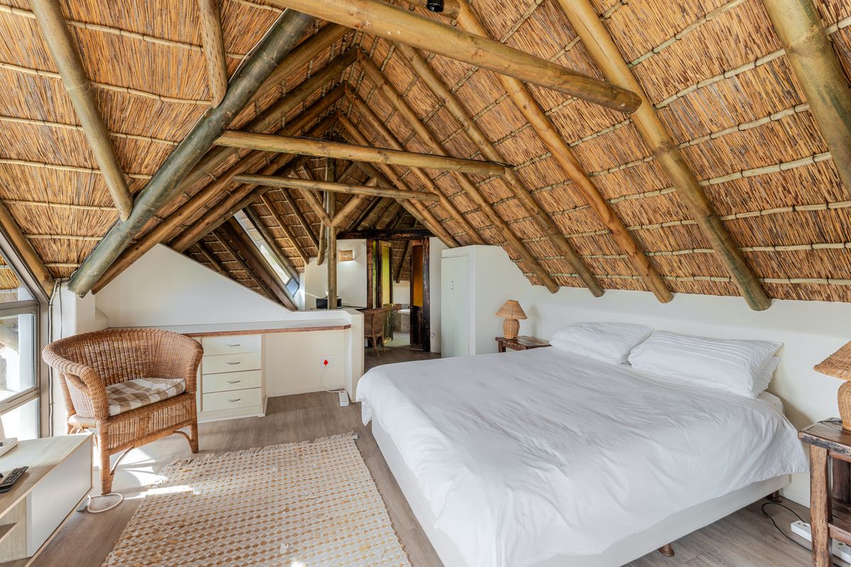 A spacious bedroom featuring a unique vaulted thatched roof with exposed timber rafters, built-in desk area, and modern laminate flooring.