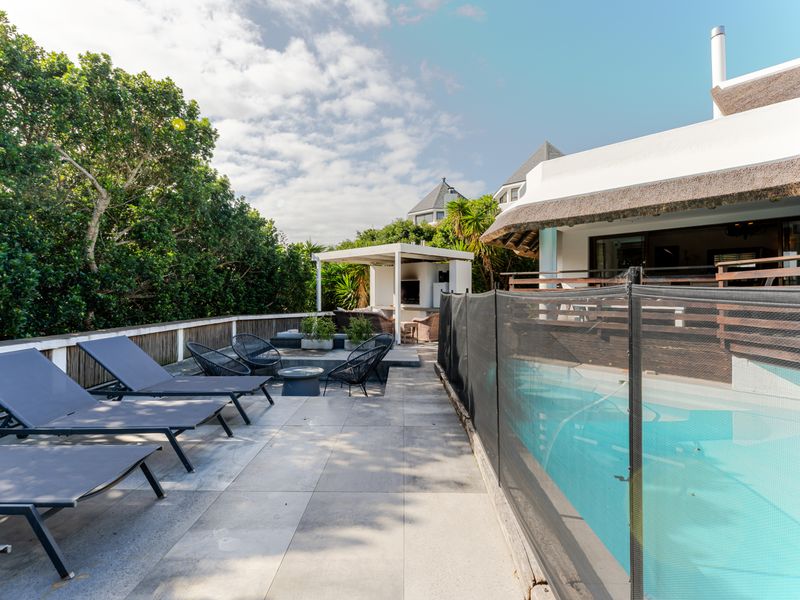 Outdoor pool area featuring a tiled patio, safety fencing, and a covered pergola with an integrated fireplace, perfect for entertaining.