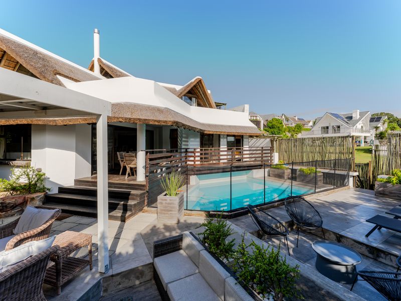Outdoor entertainment area featuring a swimming pool with safety fencing, timber decking, and a covered patio under a traditional thatched roof.
