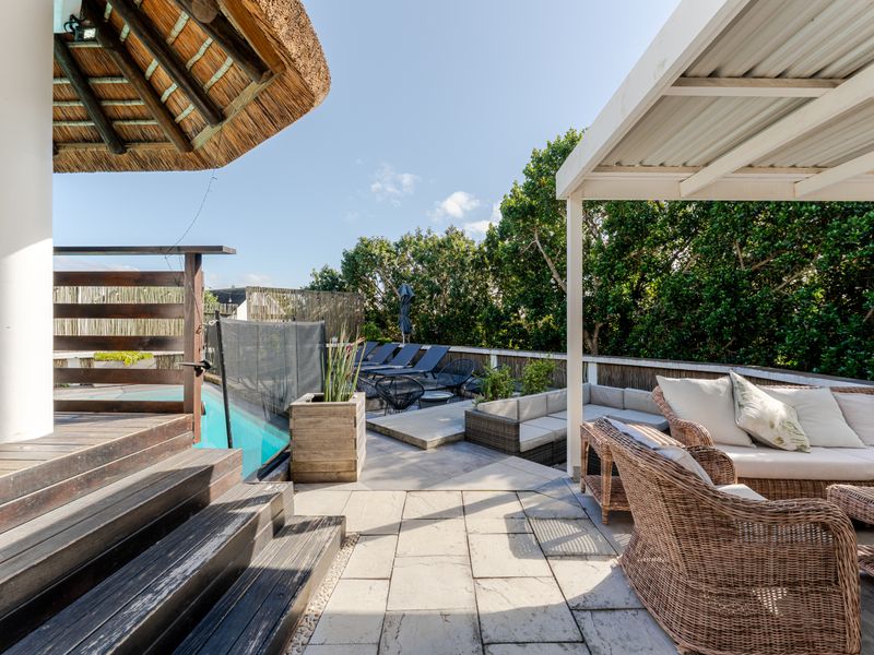 Outdoor pool area featuring a paved patio, timber decking, a thatched roof structure, and a metal pergola, perfect for relaxation and entertainment.