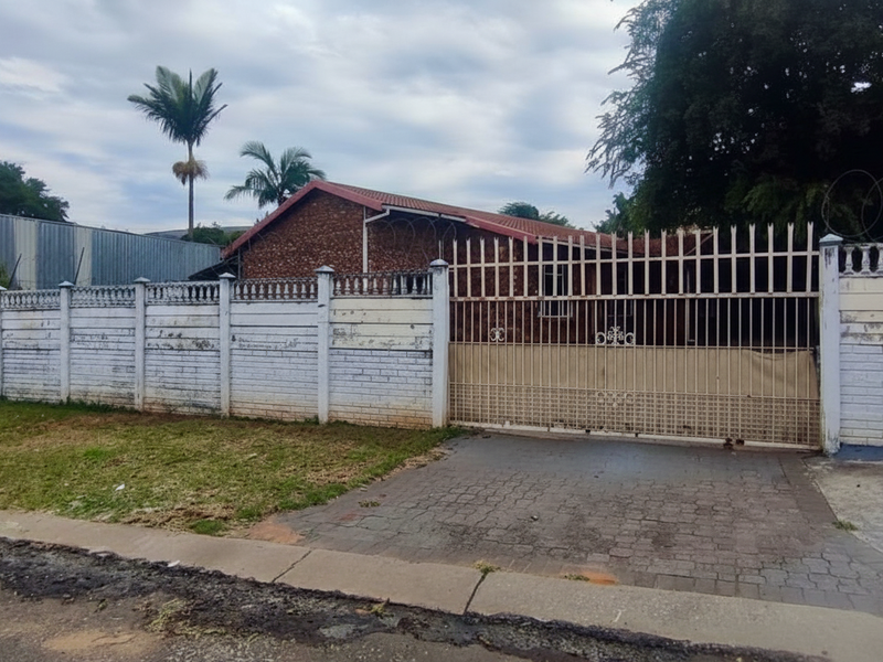 Front view of the property featuring a brick facade, tiled roof, and a secure perimeter wall with a metal gate and razor wire.