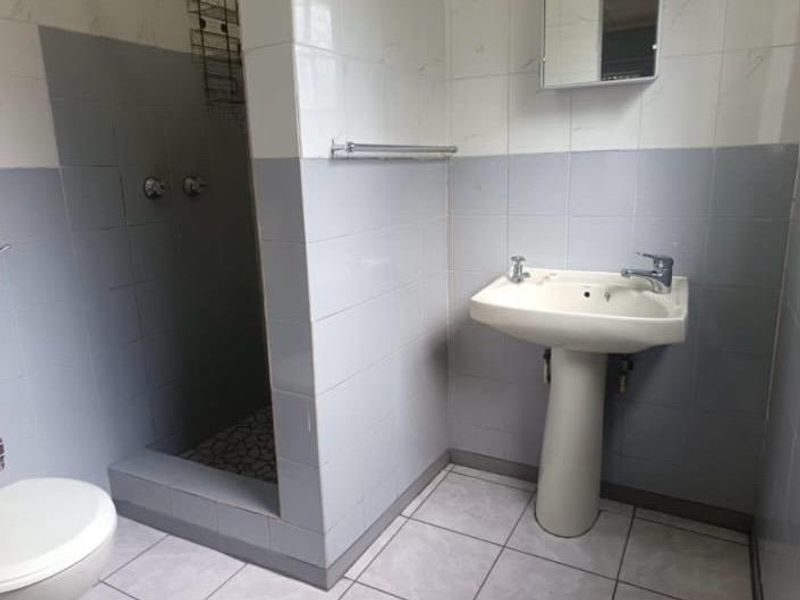 A functional bathroom featuring a pedestal basin, tiled walls, and a walk-in shower enclosure with neutral finishes.