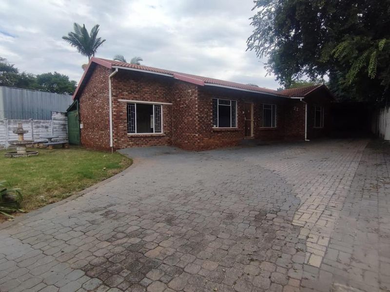 Front view of a face brick house featuring a paved driveway, tiled roof, and secure boundary walling.