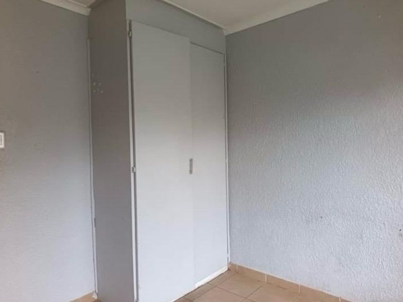 A simple, empty bedroom featuring tiled flooring and a built-in wardrobe with neutral grey walls.