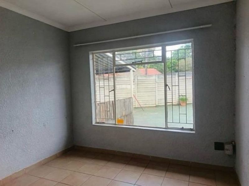 An empty bedroom featuring tiled flooring, security bars on the window, and a neutral wall finish, offering a blank canvas for personalization.