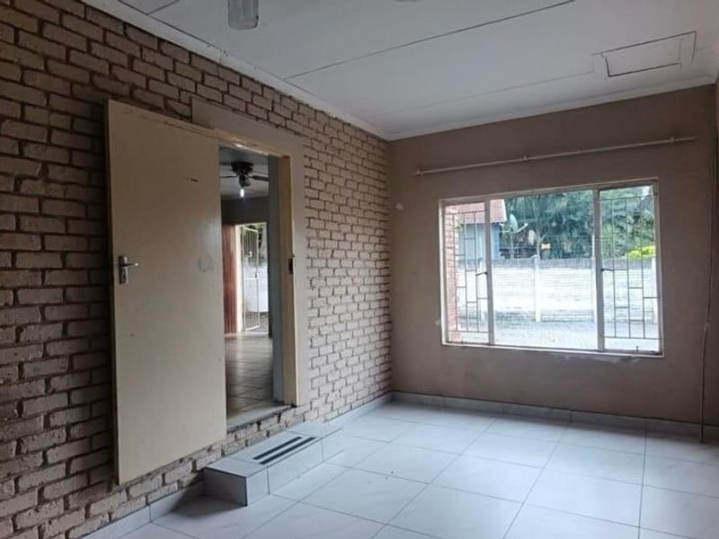 An empty living room featuring an exposed brick feature wall, tiled flooring, and large windows with security bars.