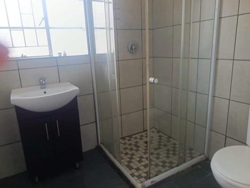 A functional bathroom featuring a corner shower enclosure, vanity basin, and tiled finishes throughout.