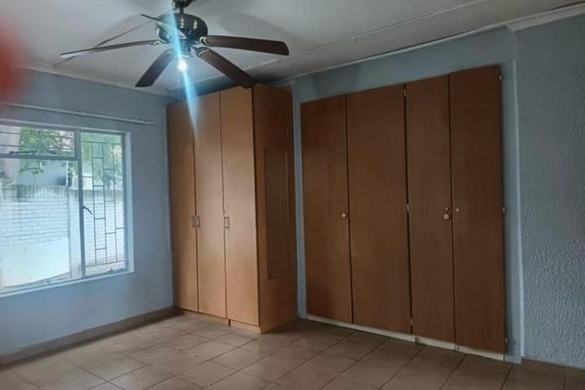 A spacious bedroom featuring extensive built-in wooden cupboards, tiled flooring, and a ceiling fan, offering a blank canvas for personalization.