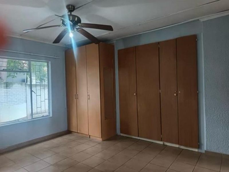 A spacious bedroom featuring extensive built-in wooden cupboards, tiled flooring, and a ceiling fan, offering a blank canvas for personalization.
