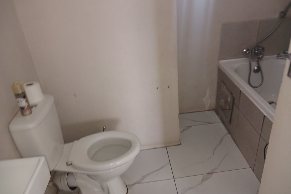 A compact bathroom featuring a standard toilet, bathtub with shower mixer, and white marble-look floor tiles.
