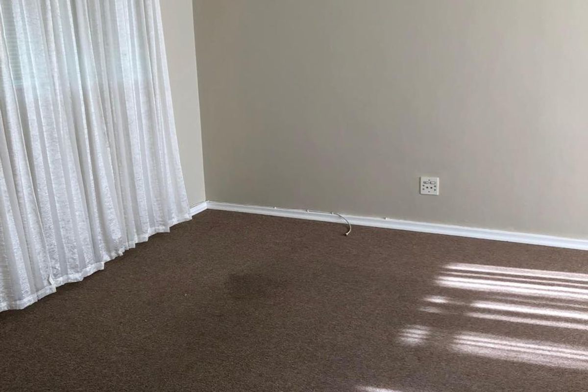 An empty bedroom featuring brown carpeting, neutral wall paint, and a curtain rod, ready for personalization.