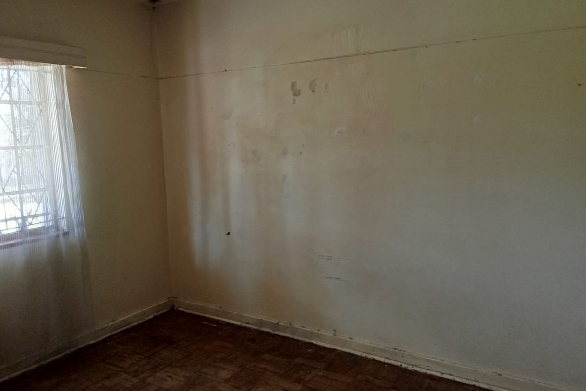 An empty bedroom featuring original parquet flooring and security bars on the window, requiring cosmetic updates to the wall finishes.