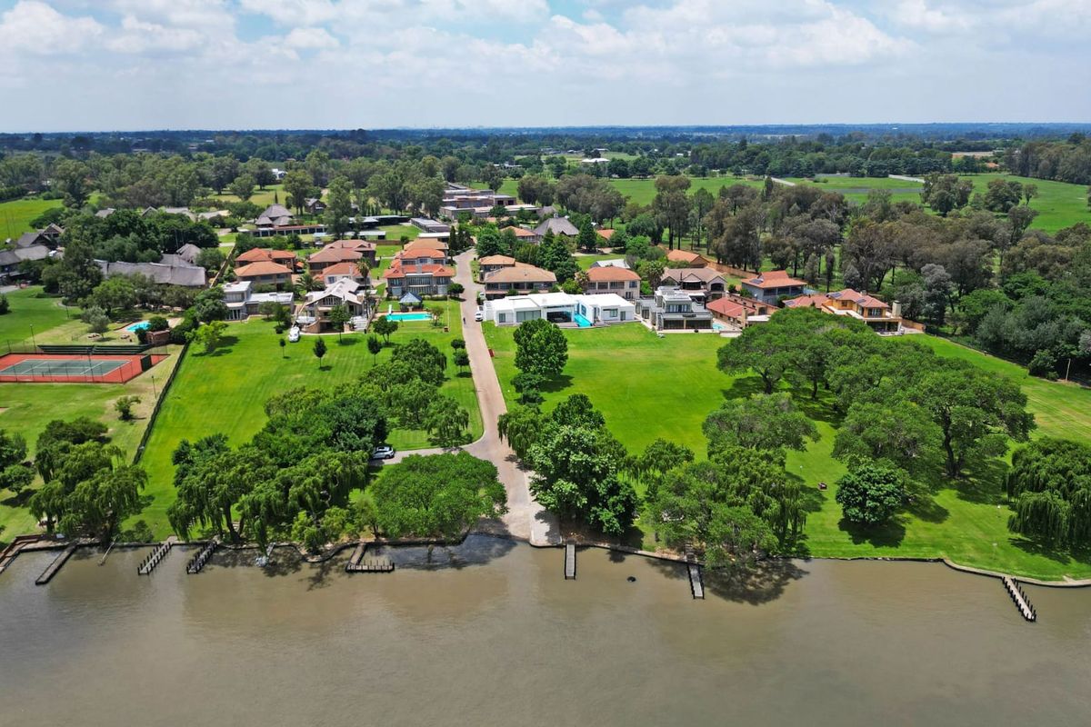 Aerial view of a residential estate featuring expansive green lawns, mature trees, and private jetty access along the waterfront.