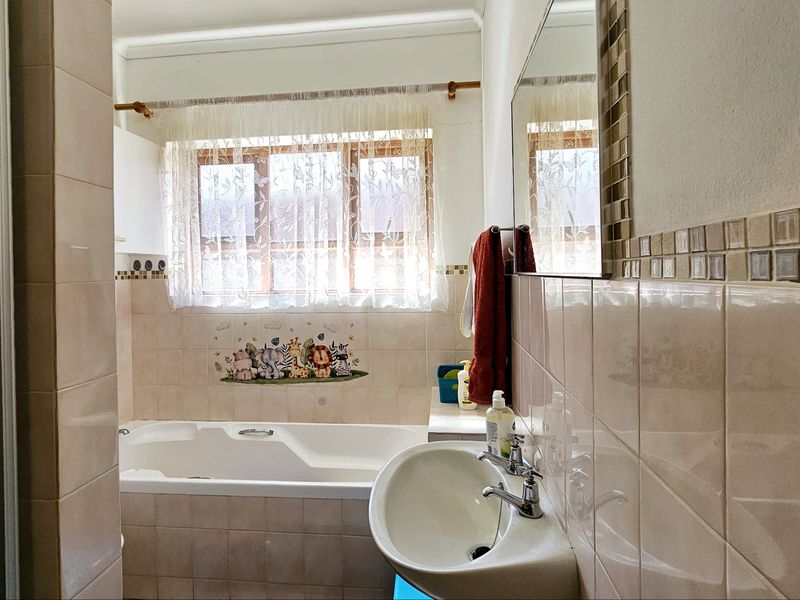 A functional bathroom featuring a built-in bathtub, wall-mounted basin, and tiled walls with a decorative mosaic border.