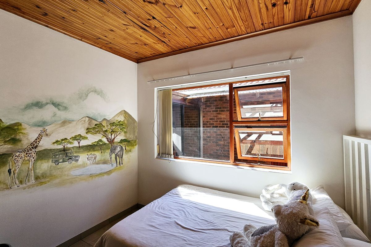 A bedroom featuring a warm timber ceiling, tiled flooring, and a top-hung timber window with a decorative wall mural.