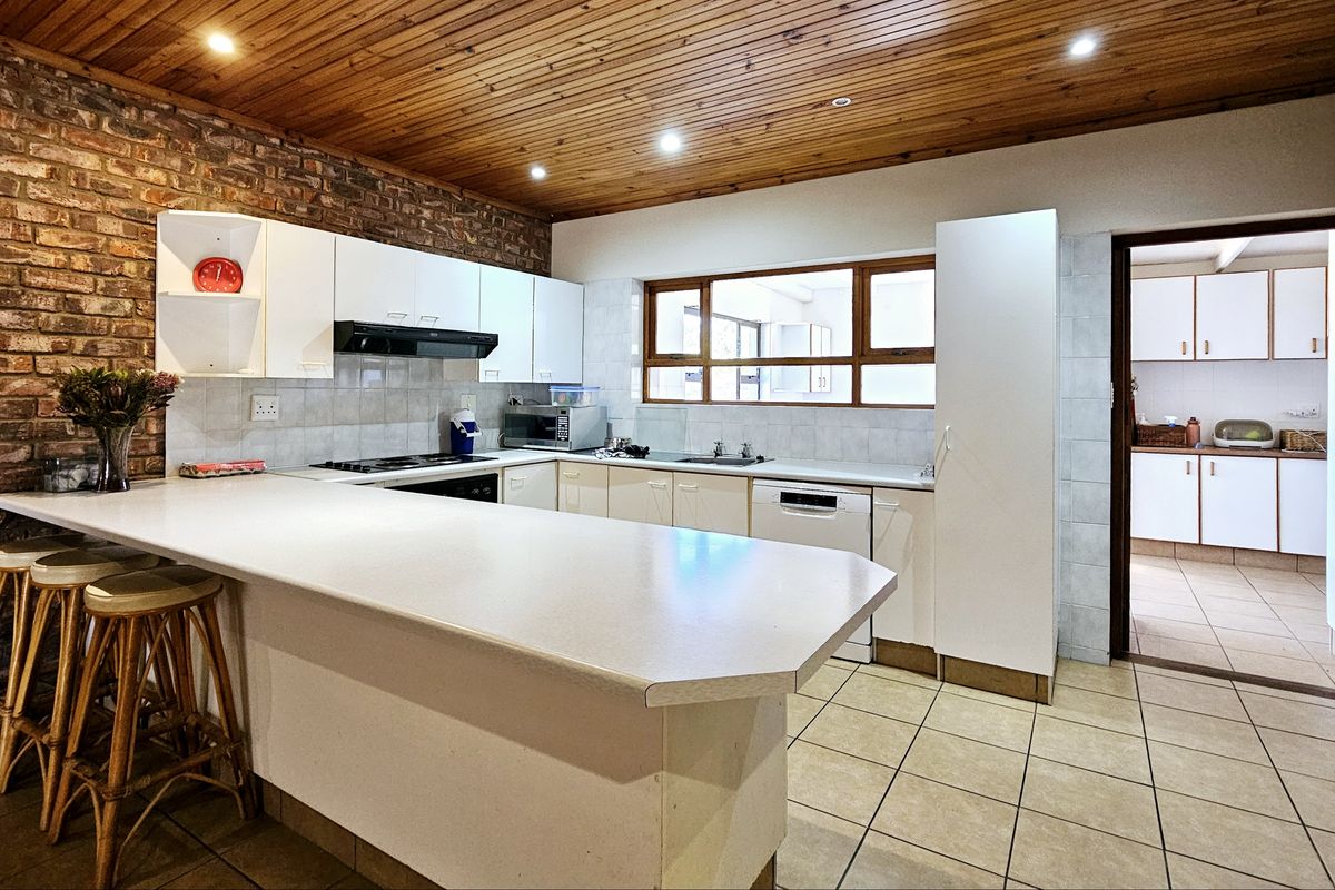 A functional kitchen featuring exposed brick walls, timber ceiling, breakfast bar, and ample built-in cabinetry, with an adjacent scullery area visible.