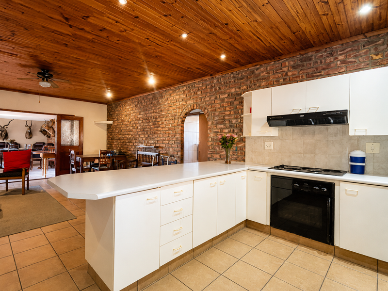 Open-plan kitchen featuring white cabinetry, built-in appliances, exposed brick wall, and timber ceiling, seamlessly flowing into the adjacent dining area.
