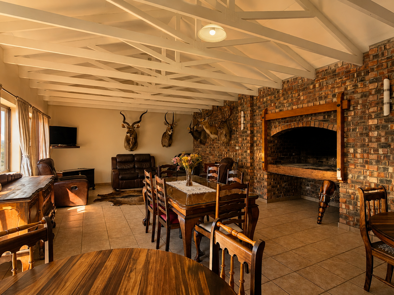 Spacious open-plan living and dining area featuring exposed timber roof trusses, a large built-in brick fireplace, and tiled flooring throughout.