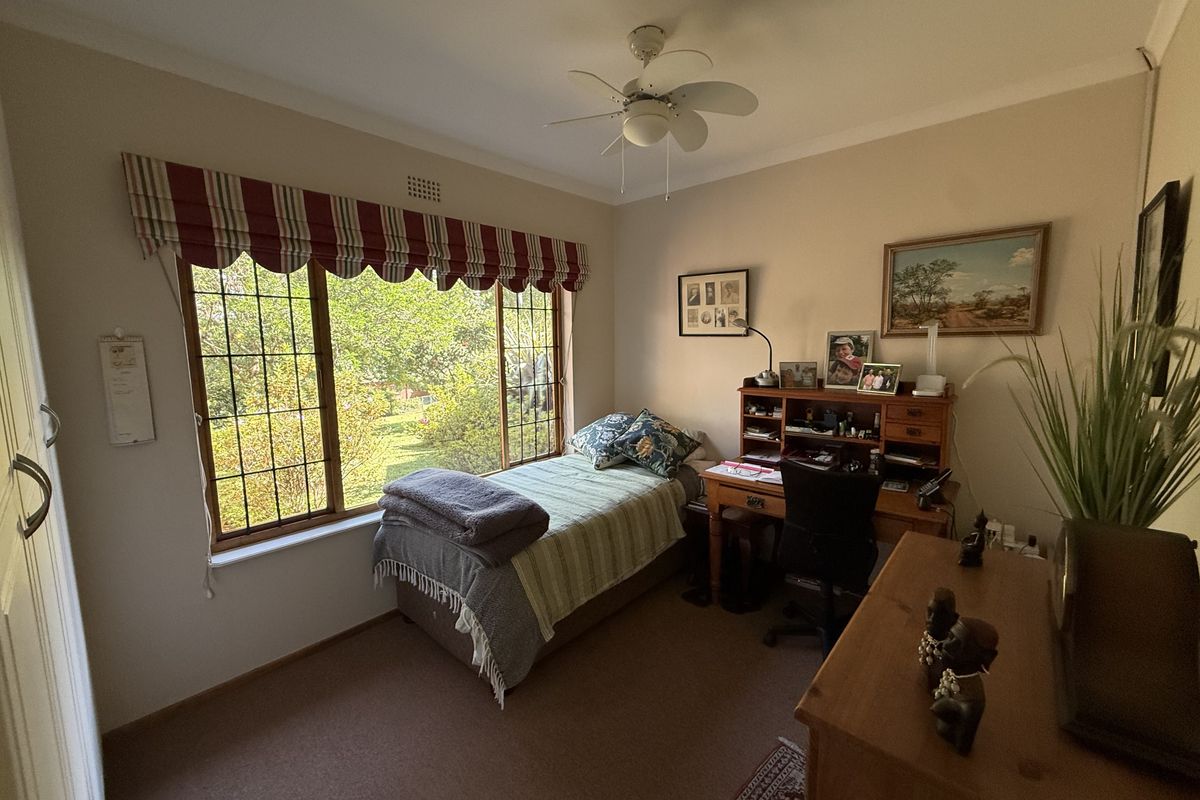A well-lit bedroom featuring a large leaded glass window, ceiling fan, and built-in storage, offering a pleasant view of the garden.