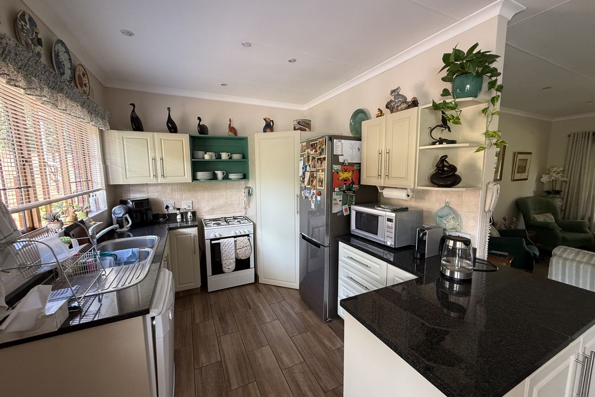 A functional kitchen featuring granite countertops, built-in cabinetry, a gas stove, and tiled flooring, offering a practical layout with an adjacent living area.