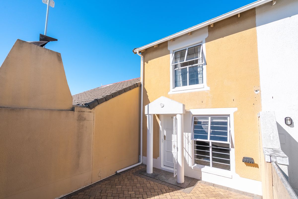 A rear courtyard area featuring paved flooring, a covered entrance portico, and sash windows set against a yellow rendered exterior wall.