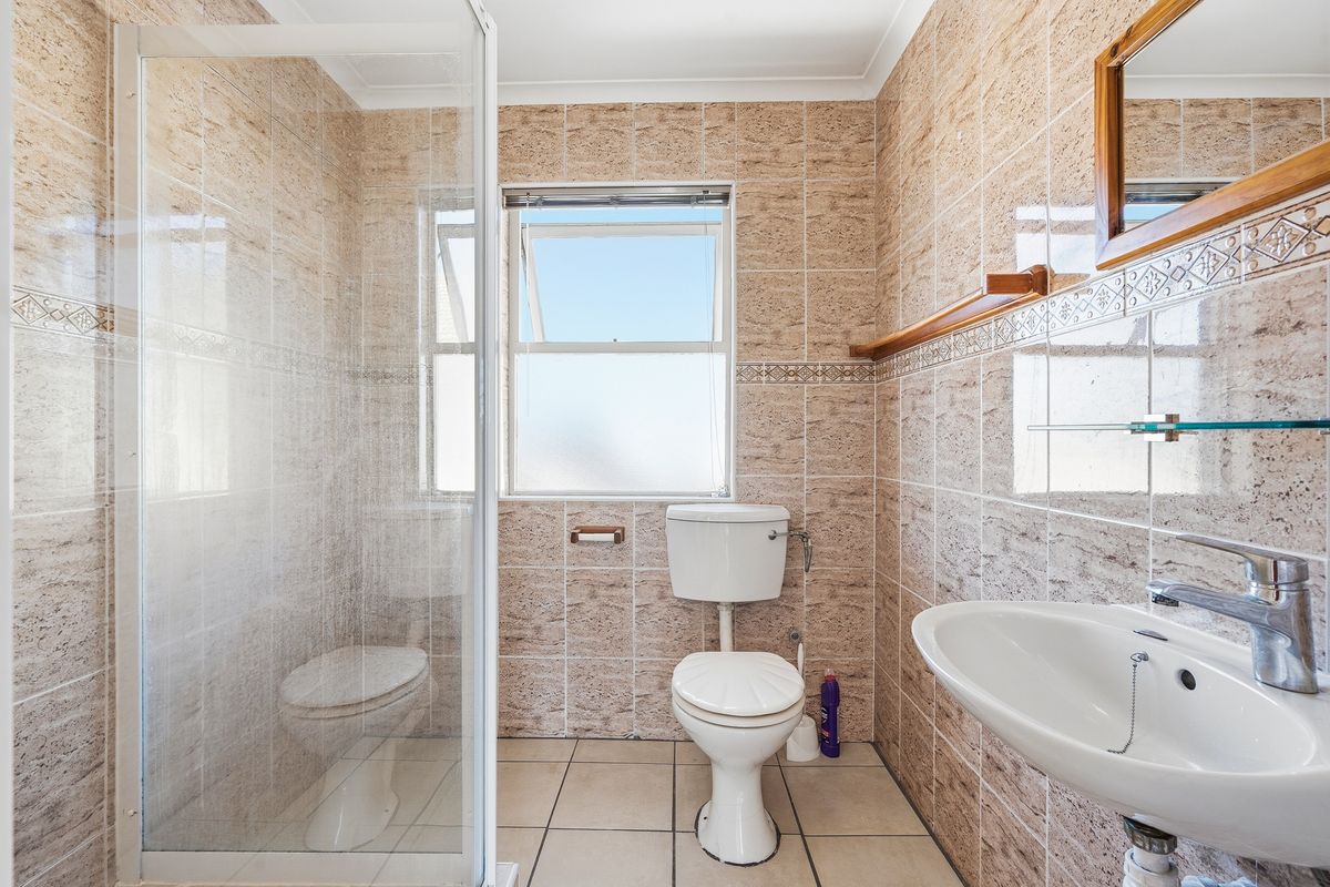 A functional bathroom featuring a shower enclosure, pedestal basin, and toilet, finished with neutral wall and floor tiling.