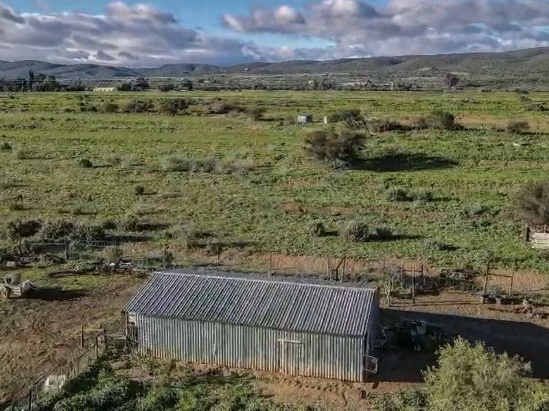 Aerial view of a rural farm property featuring a corrugated metal shed set within expansive open pasture land.