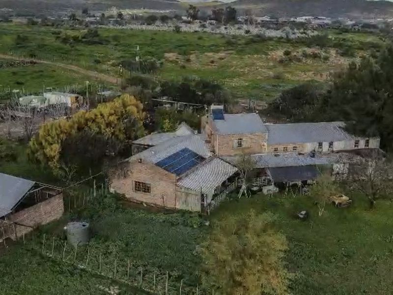 Aerial view of a rural farm property featuring brick structures, corrugated metal roofing, and installed solar panels set within a large open landscape.