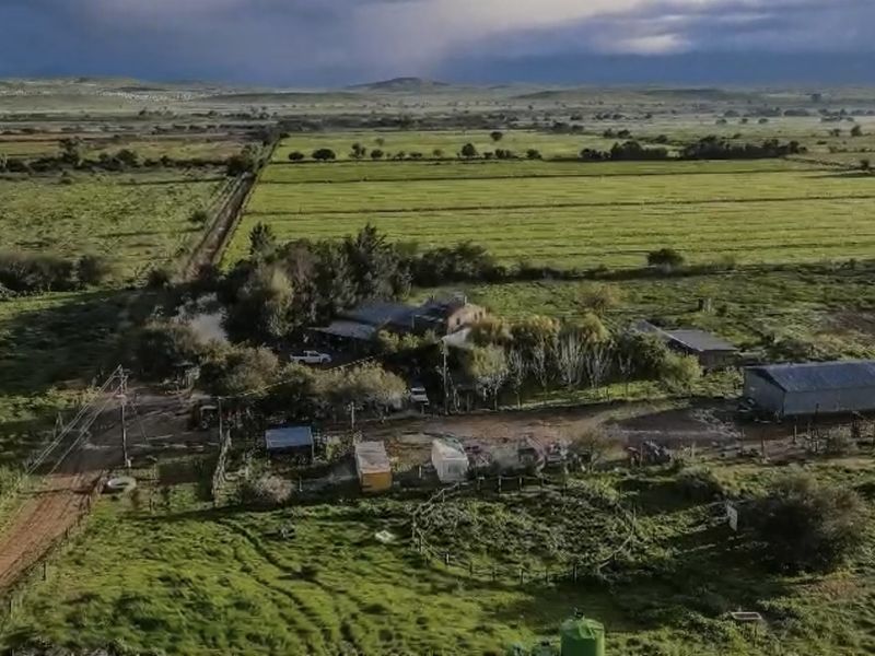 Aerial view of a rural farm property featuring multiple outbuildings, fenced paddocks, and expansive surrounding agricultural land.