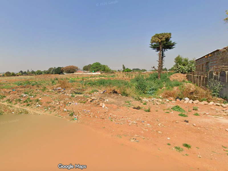 A vacant residential plot featuring unpaved access and a partial boundary wall, requiring significant site clearing and development.