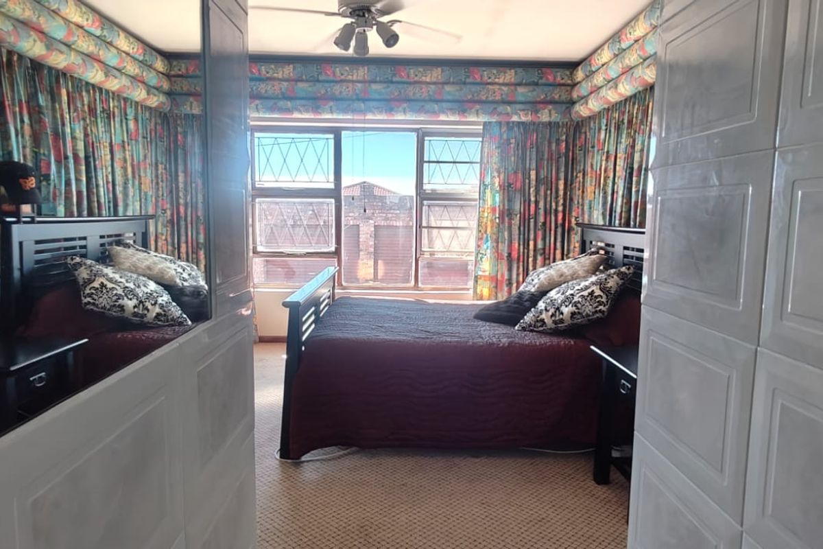 A bedroom featuring leaded glass windows, a ceiling fan, and extensive built-in cabinetry with mirrored wardrobe doors.