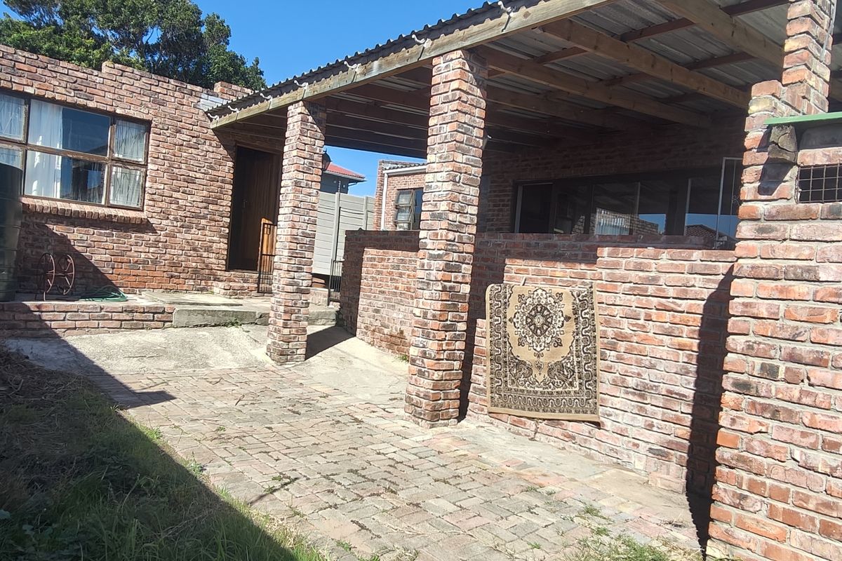 Rear exterior view featuring a brick-built structure with a covered patio area, paved courtyard, and an integrated water tank.