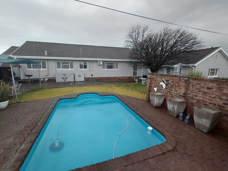 Rear exterior view featuring a swimming pool, paved patio area, and a brick boundary wall set against the rear facade of the house.