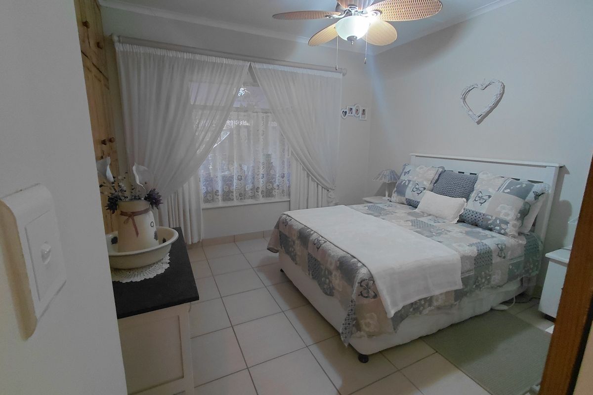 A bedroom featuring tiled flooring, a ceiling fan, and built-in cupboards, offering a functional and comfortable living space.
