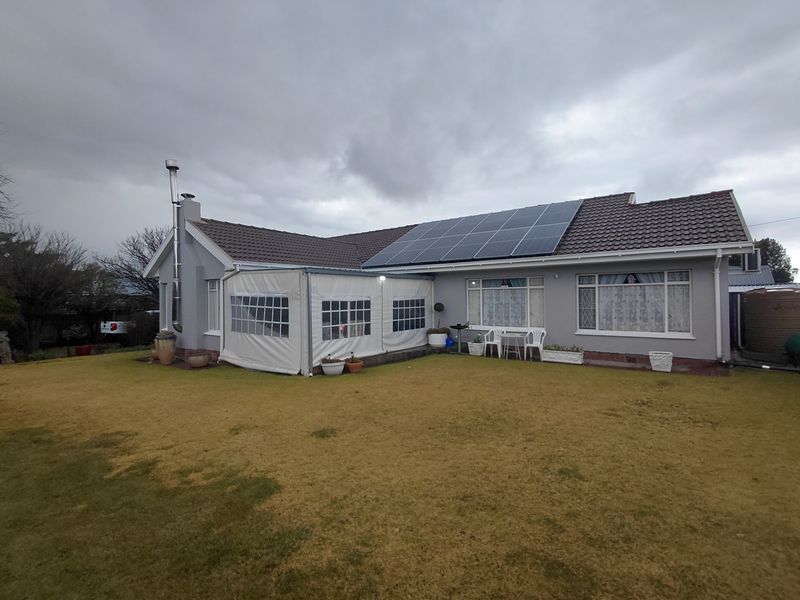 Rear view of the house featuring a tiled roof, installed solar panels, an enclosed patio area, and an external fireplace flue.
