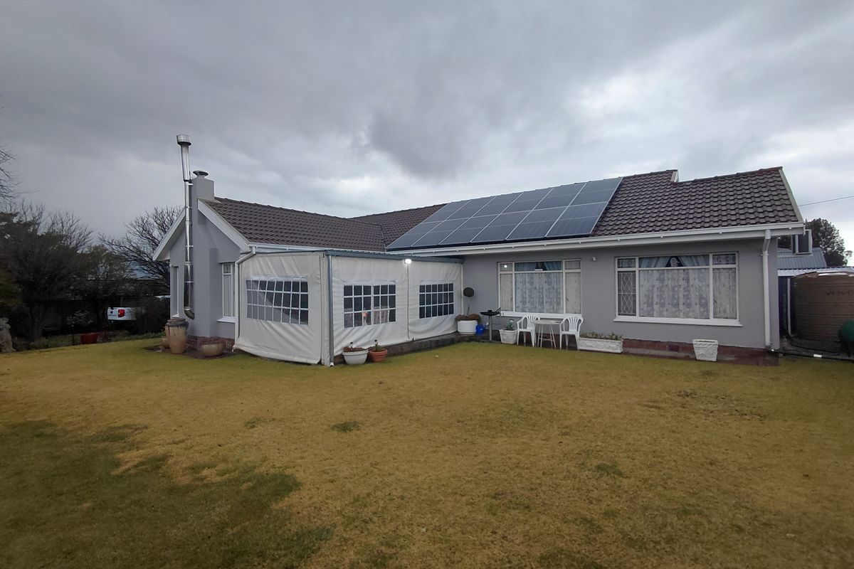 Rear view of the house featuring a tiled roof, installed solar panels, an enclosed patio area, and an external fireplace flue.