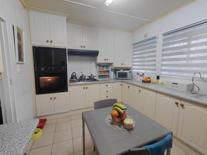 A functional kitchen featuring white cabinetry, built-in oven, gas hob, extractor fan, and tiled flooring with ample counter space and natural light.