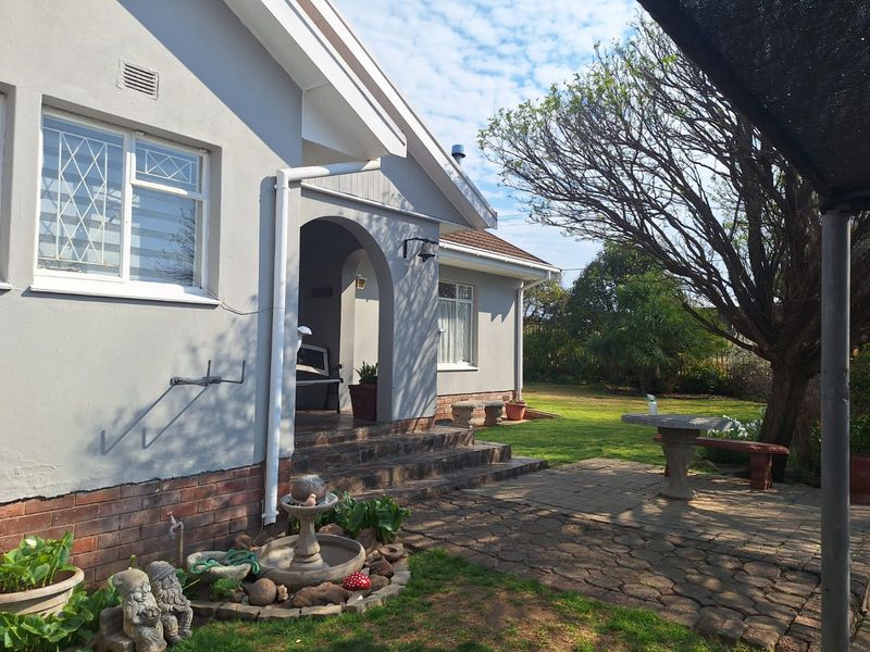 Rear view of the house featuring a paved patio area, arched entrance, and established garden surroundings.